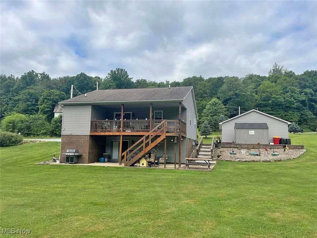 Rear view of property featuring stairs, a wooden deck, a lawn, and a view of trees