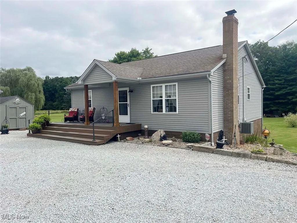 View of front of house with a storage shed, a shingled roof, a chimney, and a porch