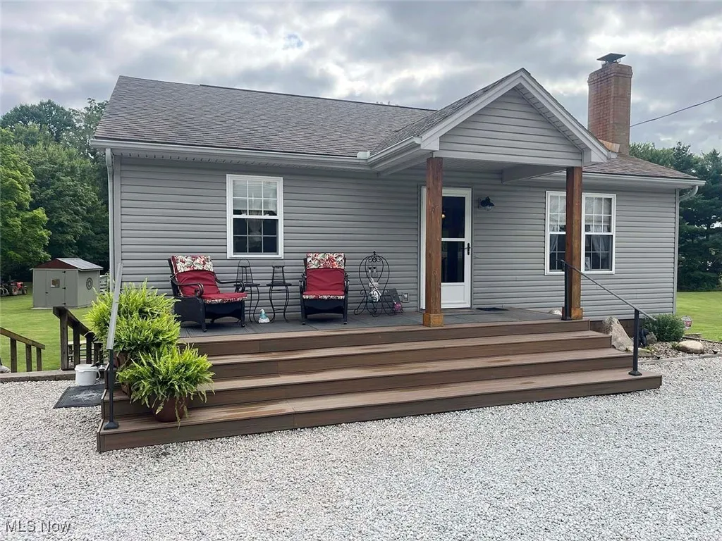 Front of house with a wooden deck, a chimney, and a shingled roof