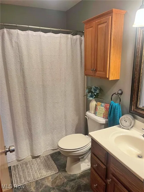 Full bath featuring vanity, stone finish floors, and curtained shower