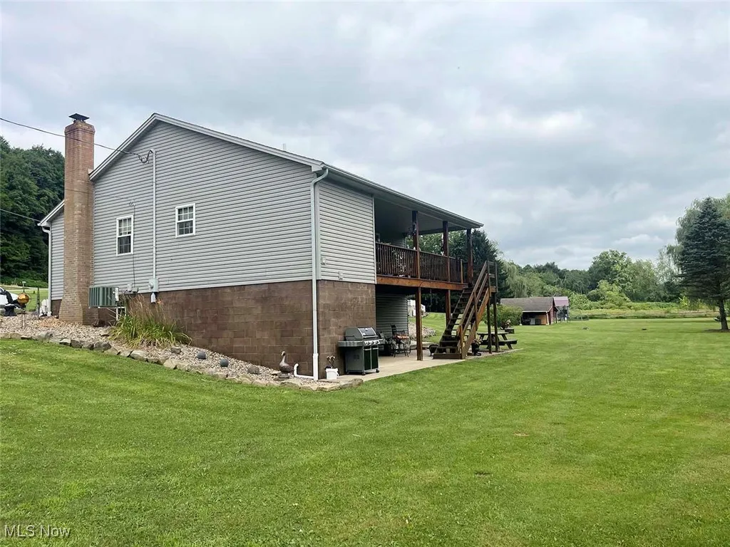 Back of property featuring a lawn, a chimney, a wooden deck, a patio area, and stairs