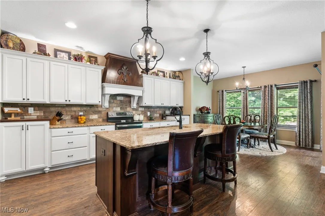 Kitchen with a chandelier, dark wood-type flooring, decorative backsplash, white cabinetry, and stainless steel electric range oven