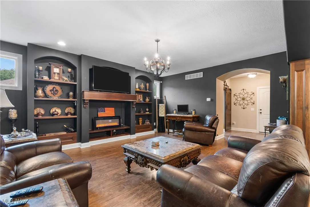 Living room with arched walkways, built in features, a glass covered fireplace, and wood finished floors