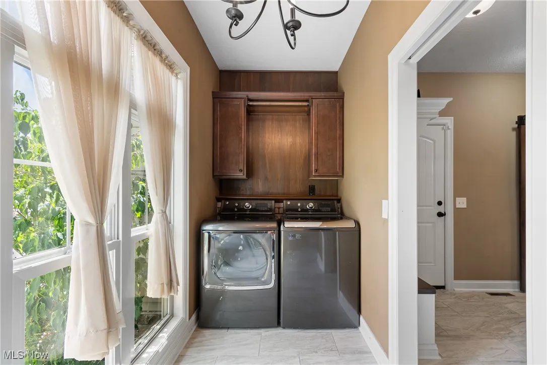 Washroom featuring separate washer and dryer, cabinet space, a chandelier, light marble finish flooring, and plenty of natural light