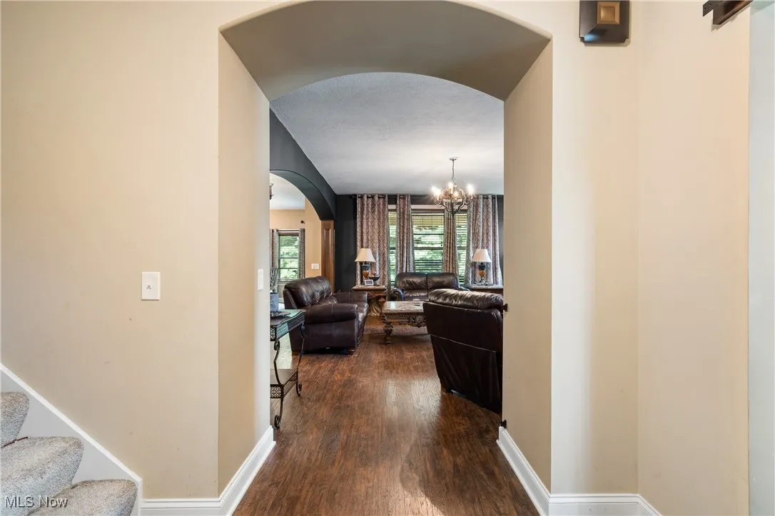 Hallway featuring arched walkways, dark wood-style floors, a chandelier, and stairway
