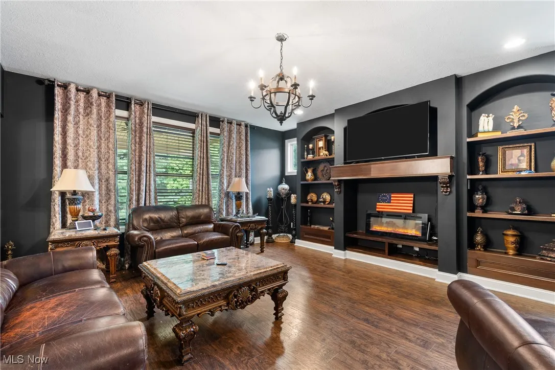Living room with a chandelier, built in features, wood finished floors, and a glass covered fireplace