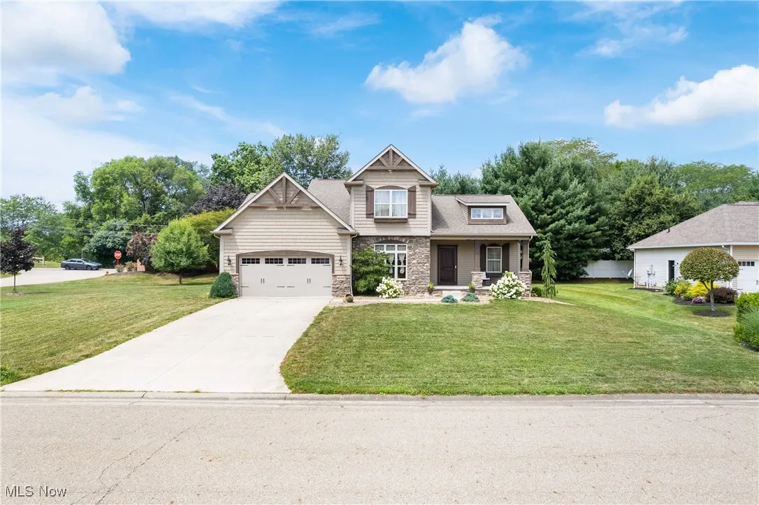 Craftsman-style home with driveway, a front yard, stone siding, and an attached garage