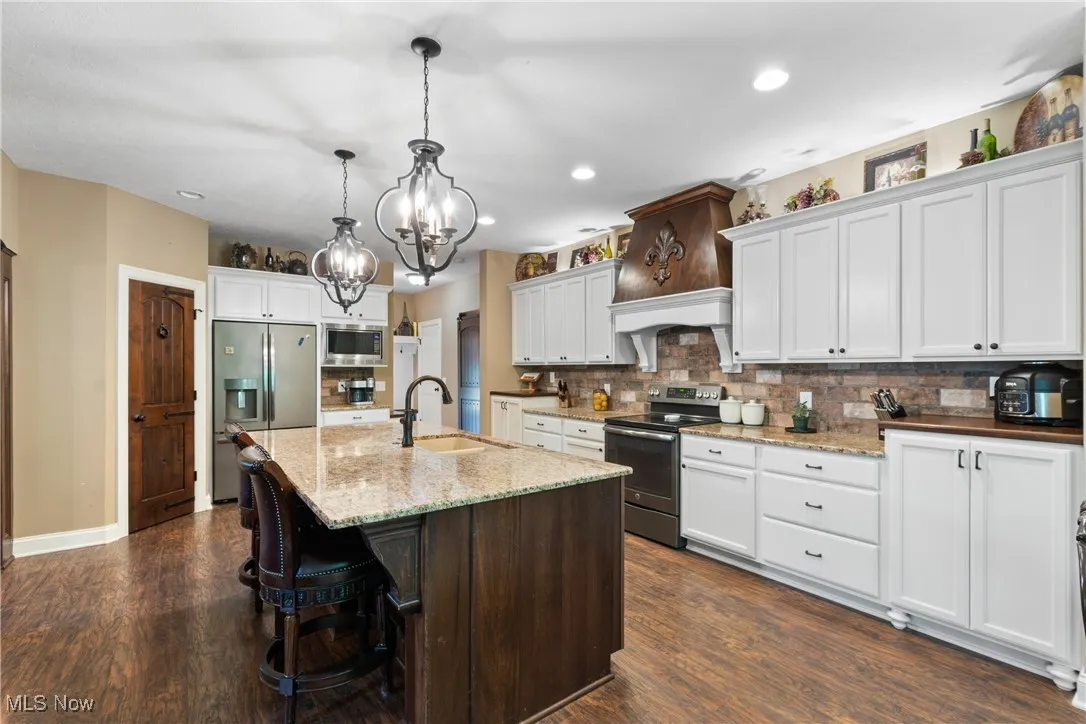 Kitchen featuring a chandelier, appliances with stainless steel finishes, dark wood-type flooring, decorative backsplash, and white cabinets