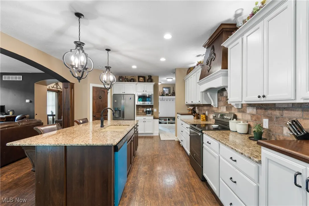 Kitchen with arched walkways, appliances with stainless steel finishes, white cabinetry, decorative backsplash, and recessed lighting
