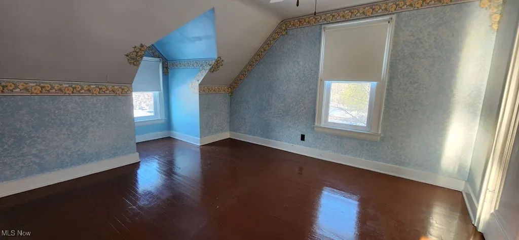 Additional living space with wood finished floors, vaulted ceiling, wallpapered walls, and a ceiling fan