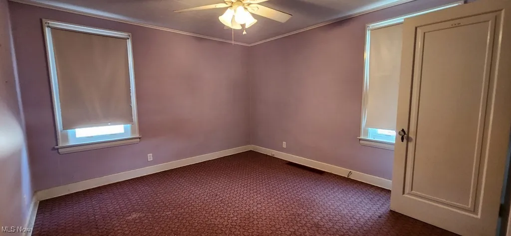Empty room featuring ceiling fan, dark colored carpet, and ornamental molding