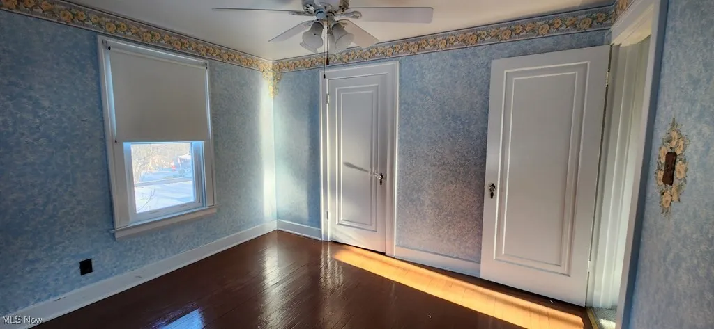 Spare room featuring dark wood finished floors, ceiling fan, and wallpapered walls