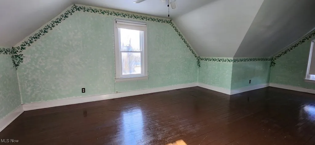 Additional living space featuring dark wood-type flooring, lofted ceiling, a ceiling fan, and wallpapered walls