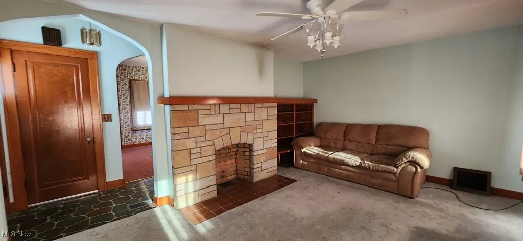 Living room featuring carpet floors, a ceiling fan, a fireplace, and arched walkways
