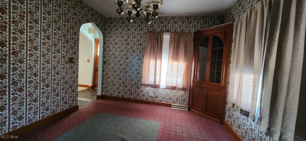 Unfurnished dining area featuring wallpapered walls, arched walkways, and a chandelier