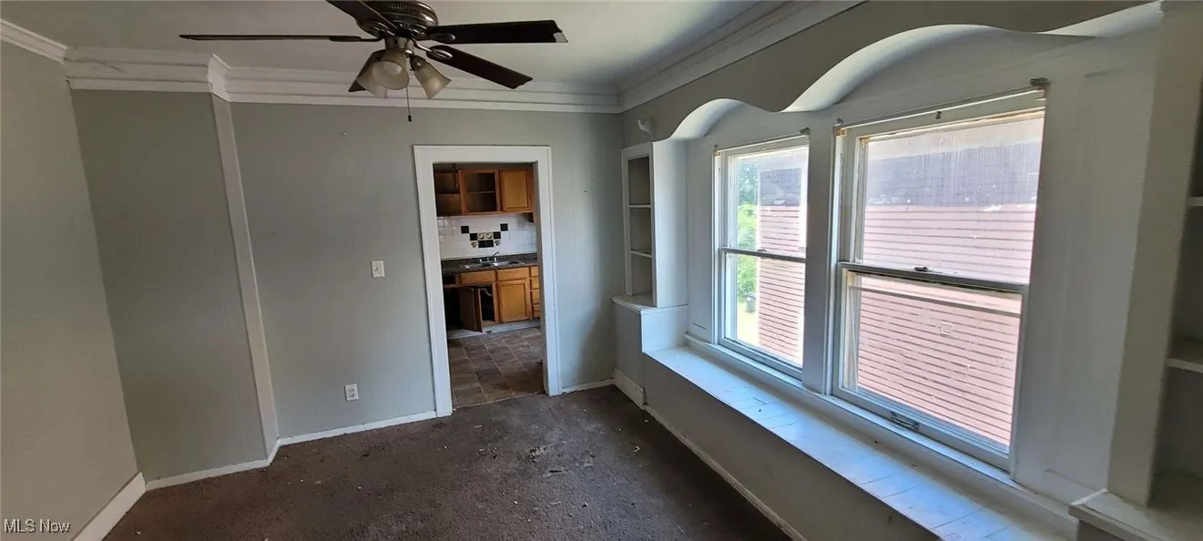 Empty room with crown molding, plenty of natural light, and ceiling fan