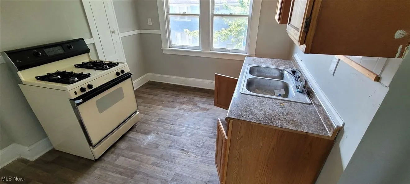 Kitchen with white range with gas stovetop, wood finished floors, and brown cabinetry