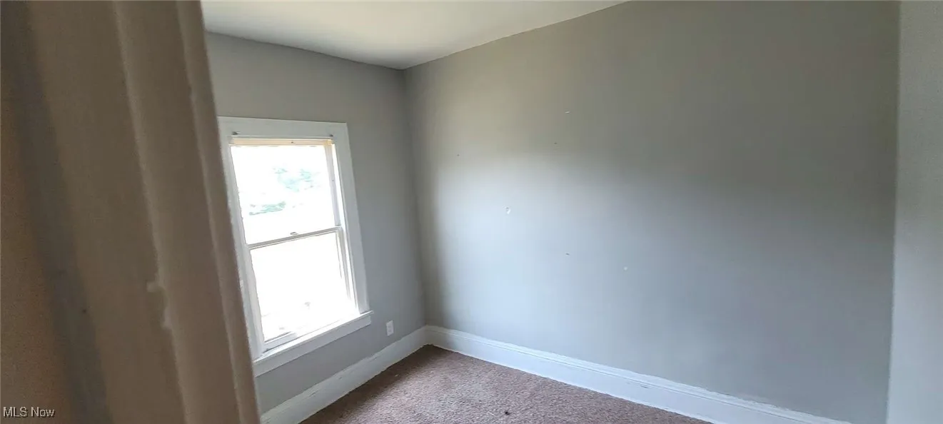 Spare room featuring dark colored carpet and baseboards