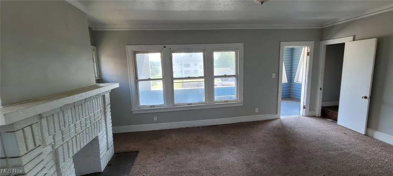 Unfurnished living room with carpet flooring, ornamental molding, and a fireplace