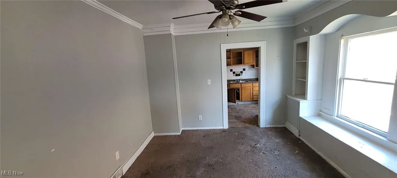 Spare room featuring plenty of natural light, a ceiling fan, ornamental molding, and unfinished concrete floors