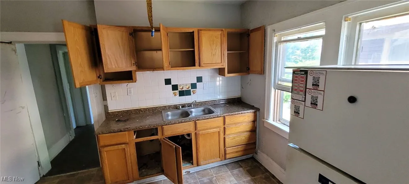 Kitchen with freestanding refrigerator, open shelves, backsplash, and dark countertops