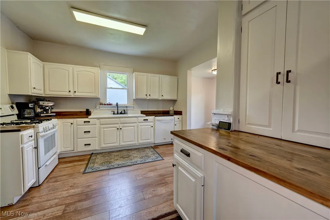 Kitchen with butcher block countertops, white appliances, light wood-type flooring, and white cabinetry