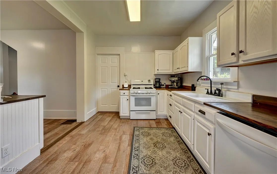 Kitchen with white appliances, light wood-style floors, white cabinetry, and butcher block countertops