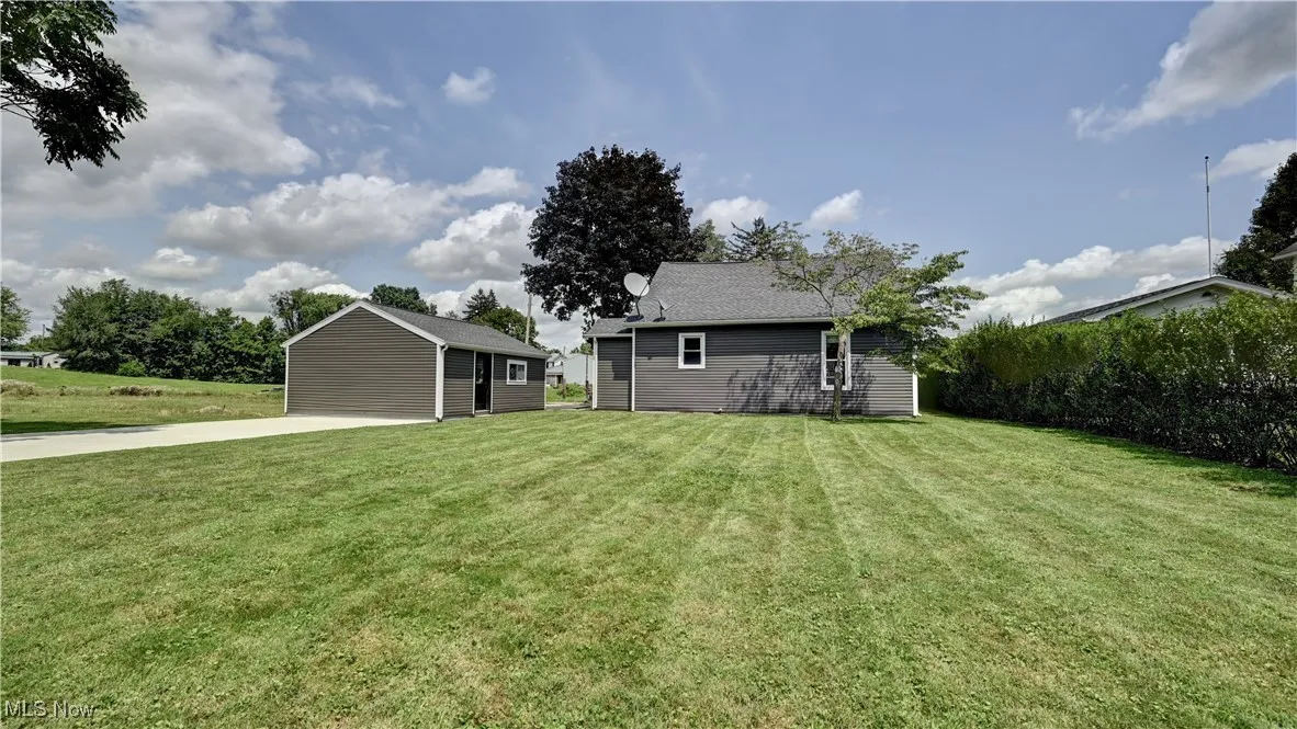 View of green lawn featuring an outbuilding, driveway, and a garage
