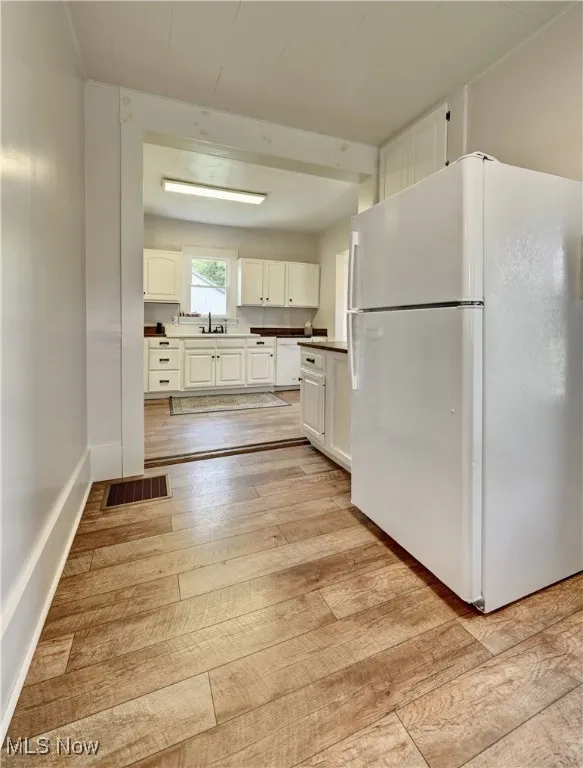 Kitchen with white appliances, light wood-style floors, and white cabinetry
