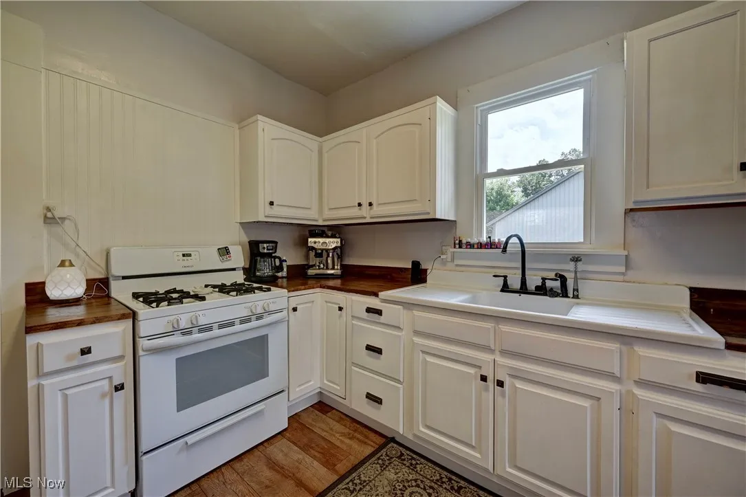 Kitchen featuring white gas stove, white cabinetry, and light wood finished floors
