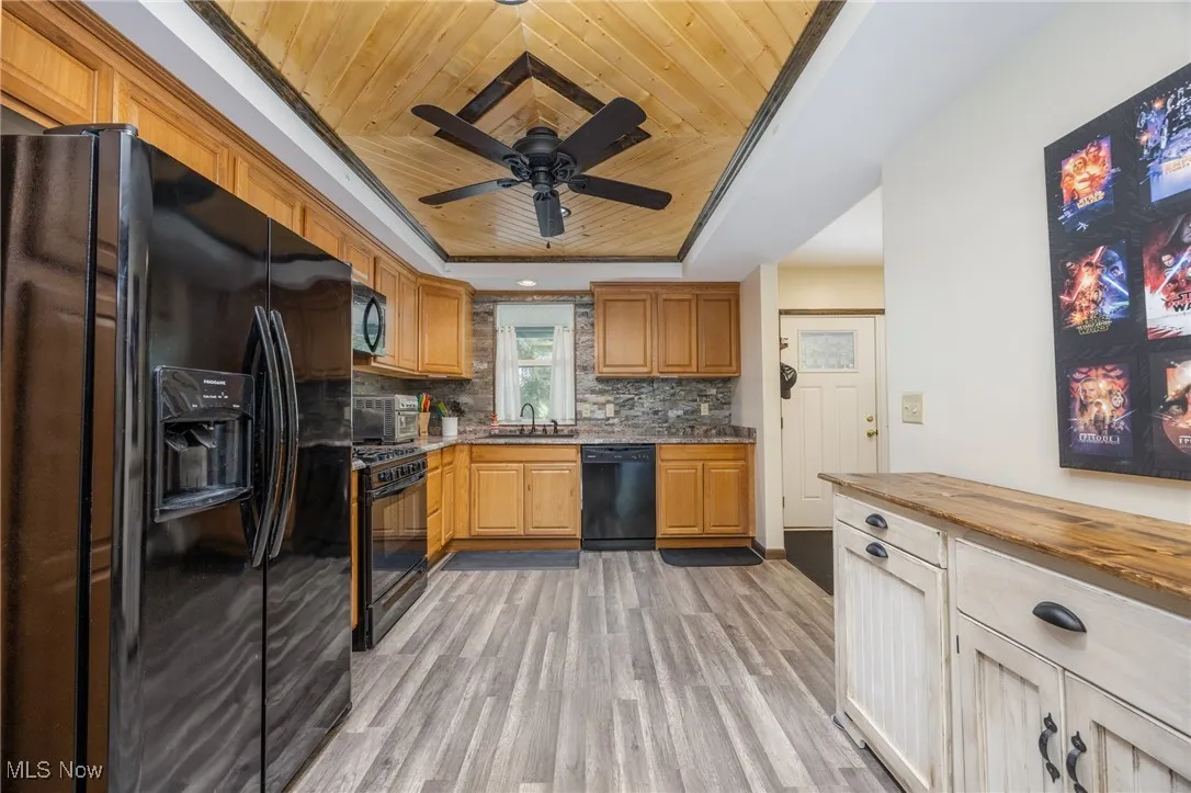 Kitchen with a raised ceiling, black appliances, wood ceiling, light wood-type flooring, and ceiling fan
