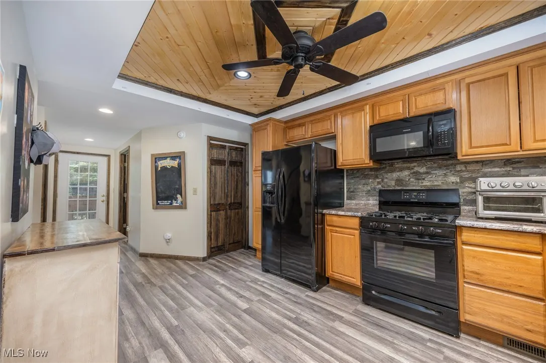 Kitchen featuring black appliances, a raised ceiling, backsplash, light wood-type flooring, and wooden ceiling