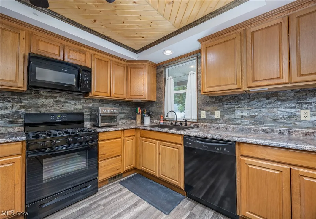 Kitchen featuring black appliances, wood ceiling, light wood-type flooring, backsplash, and ornamental molding