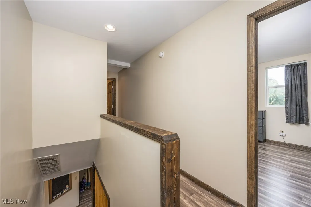 Corridor with an upstairs landing, wood finished floors, and recessed lighting