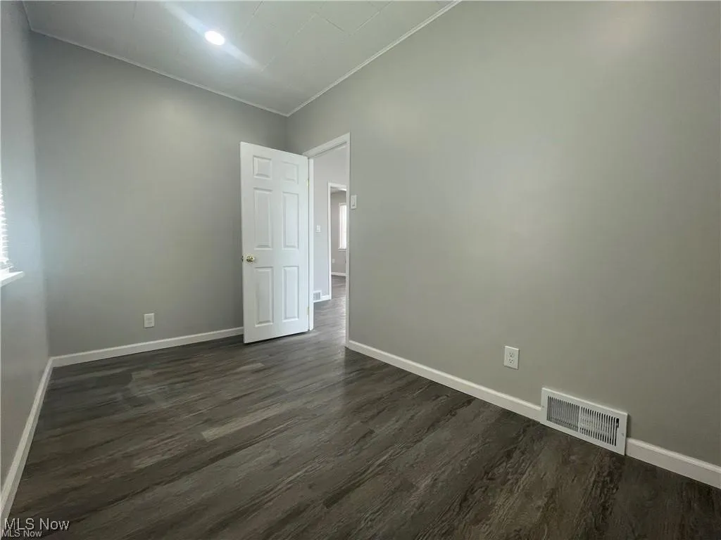 Spare room featuring dark wood-style floors and crown molding