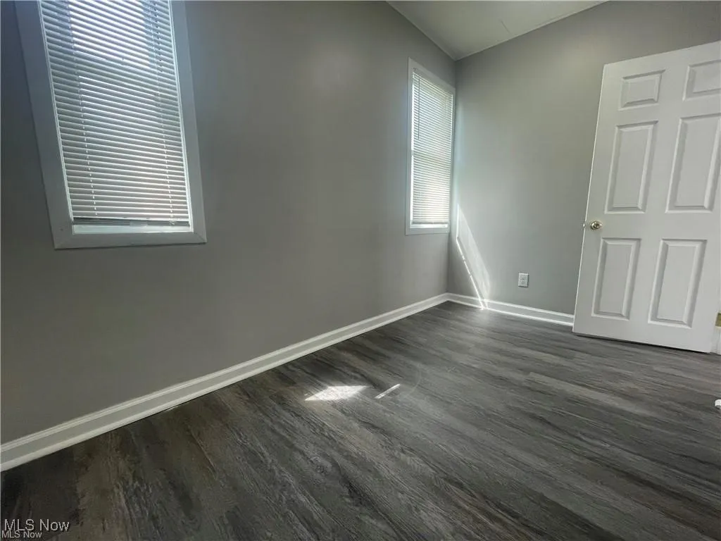 Empty room featuring dark wood finished floors and baseboards