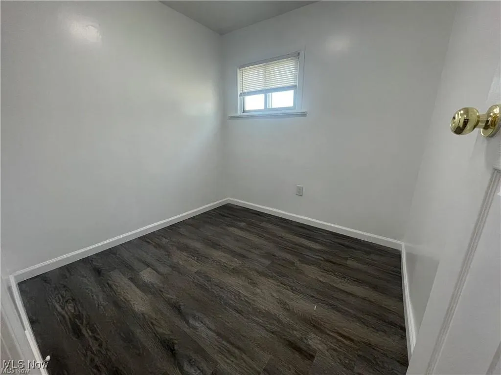 Unfurnished room featuring baseboards and dark wood-style floors