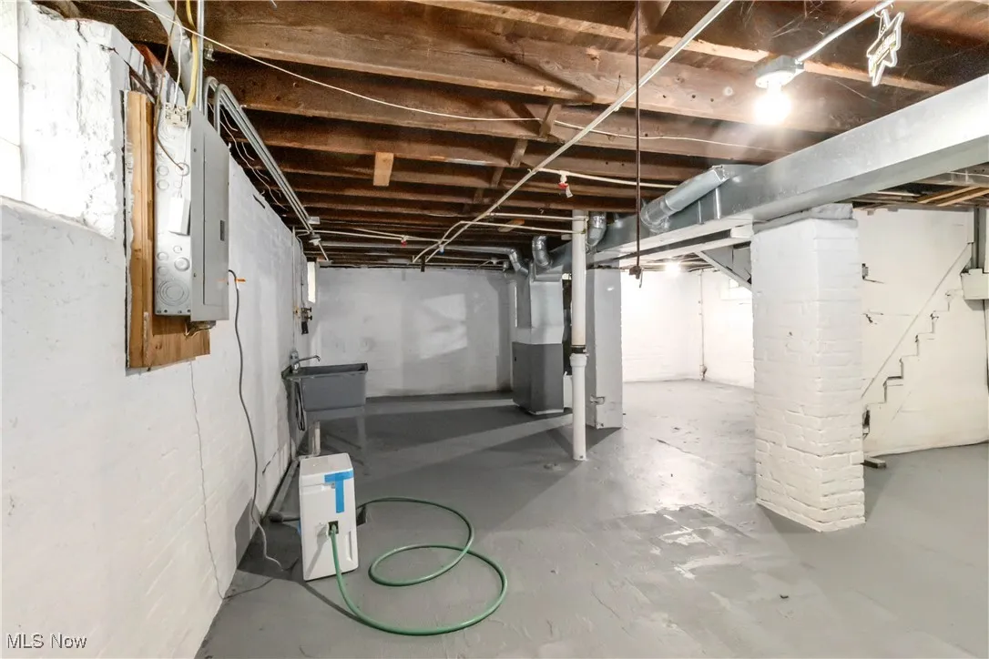 Unfinished below grade area featuring electric panel, stairway, and heating unit
