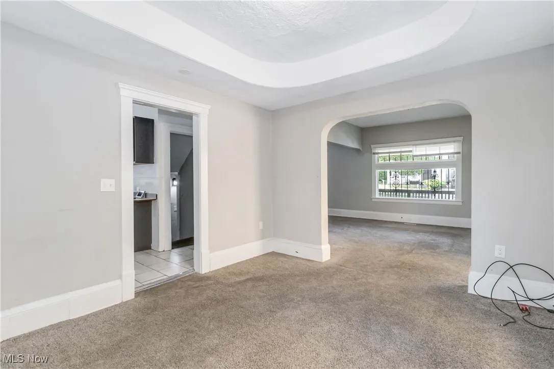 Spare room featuring arched walkways, carpet, and a raised ceiling