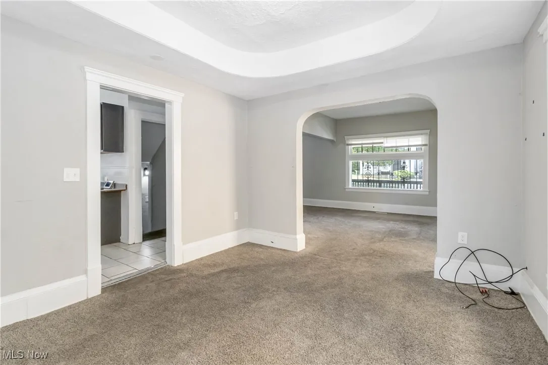 Unfurnished room with arched walkways, carpet floors, and a raised ceiling