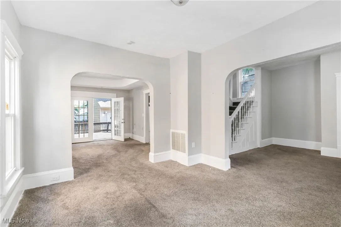 Empty room with arched walkways, carpet flooring, and stairs