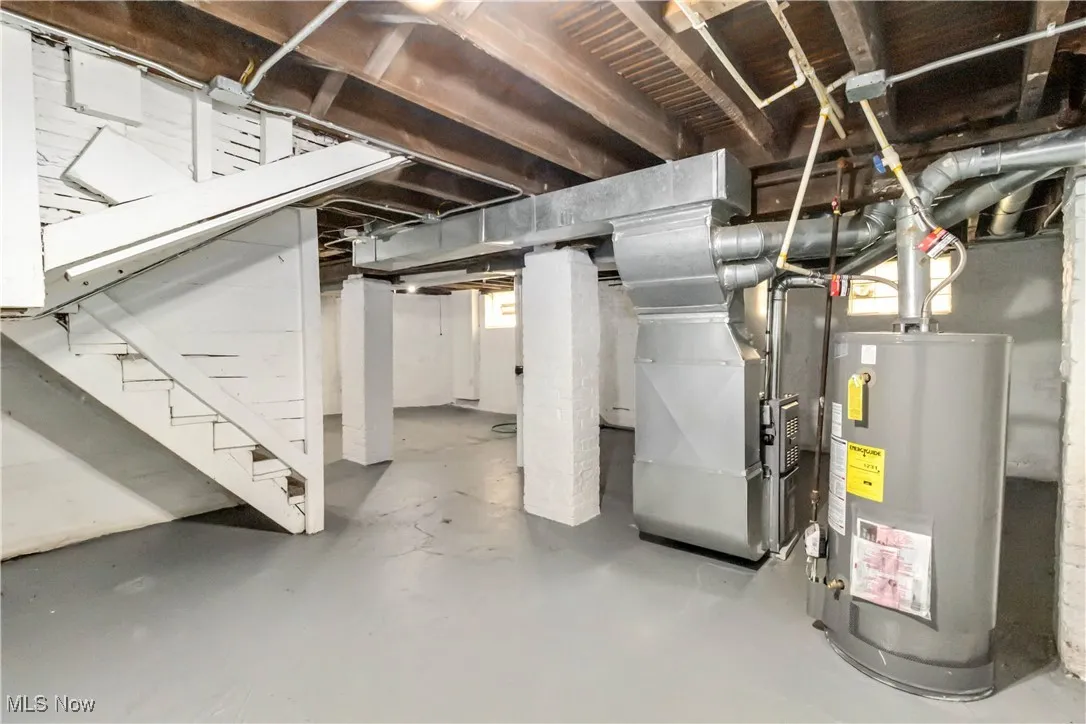 Unfinished below grade area featuring gas water heater, heating unit, and stairs