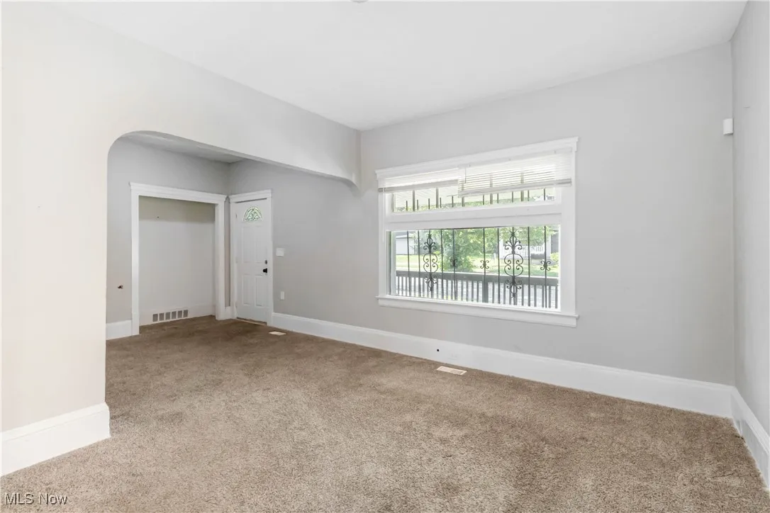 Carpeted spare room featuring arched walkways and baseboards