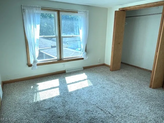 Unfurnished bedroom featuring carpet floors, a baseboard radiator, and a closet
