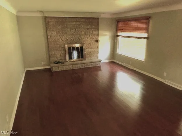 Unfurnished living room featuring dark wood-style flooring and a stone fireplace