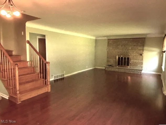 Unfurnished living room with stairs, wood finished floors, a chandelier, and a stone fireplace