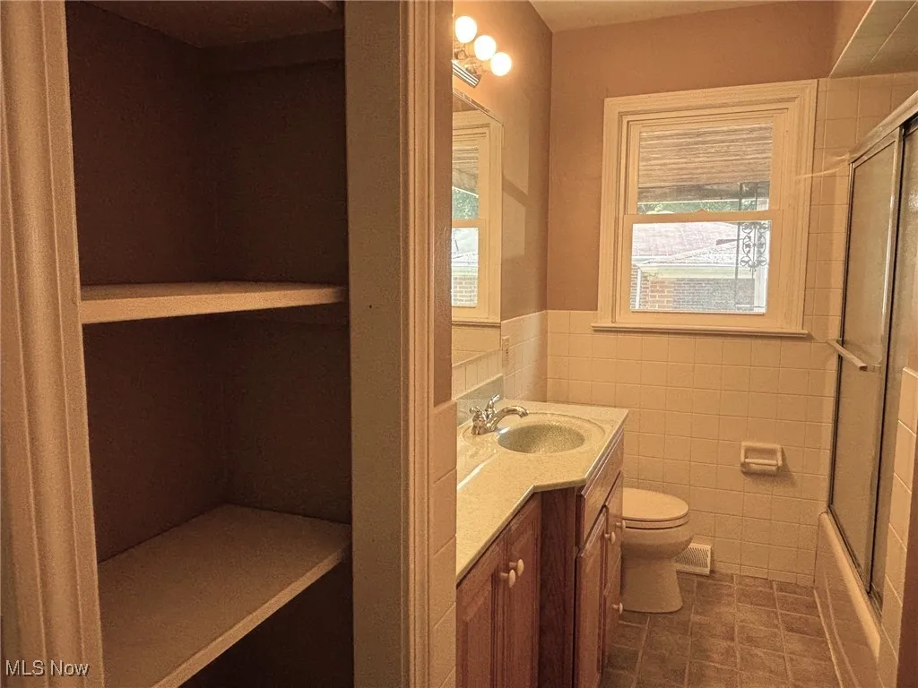 1st floor Bathroom featuring vanity, a wainscoted wall, tile patterned floors, shower / bath combination with glass door, and tile walls