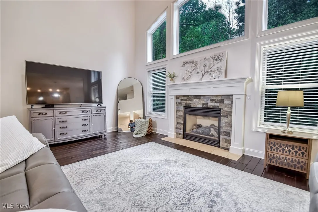 Living room with wood finished floors, a stone fireplace, and a towering ceiling