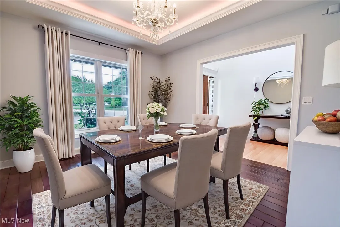Dining area with dark wood finished floors, a chandelier, and crown molding - Virtually staged