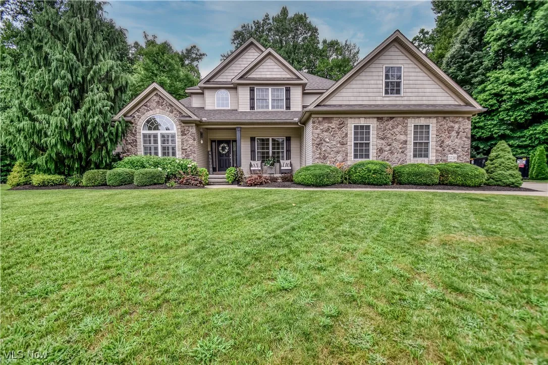 View of front of home featuring stone siding, covered porch, and a front yard